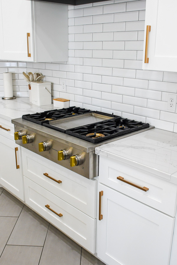 Stainless gas range with brass knobs against a white subway-tile backsplash and marble counters