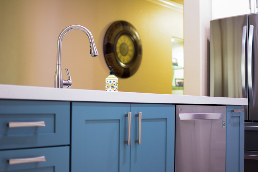 Kitchen detail with blue lower cabinets, white quartz counter, and a brushed-steel faucet