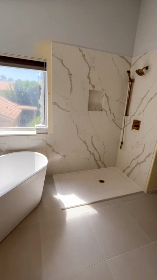 Master bathroom with a freestanding soaking tub, marble-look walk-in shower, and brass fixtures