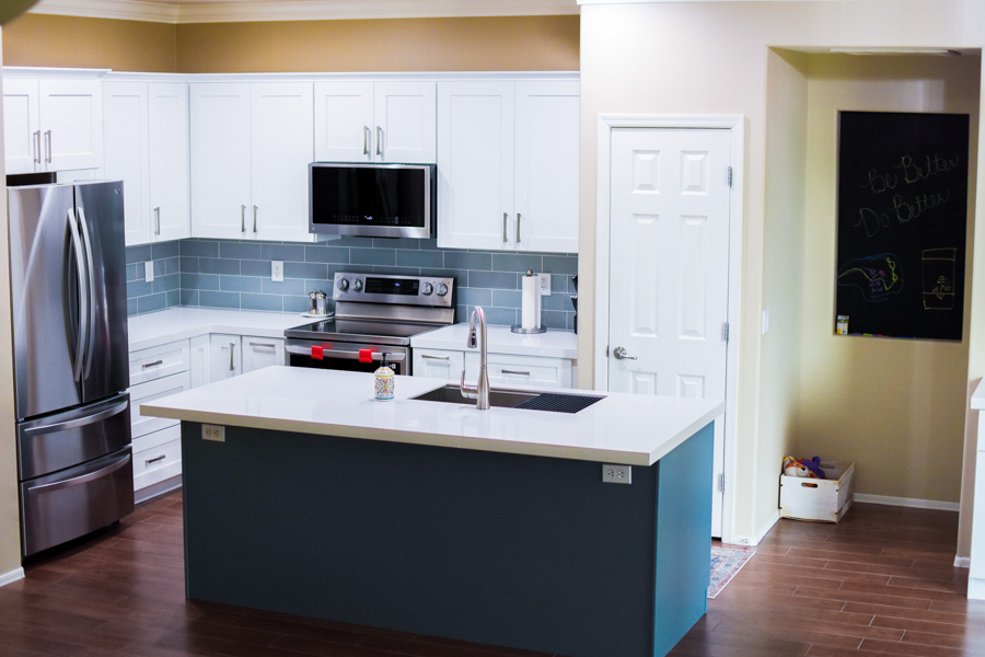 Open-concept kitchen and dining area with white cabinets, a navy island, and stainless appliances